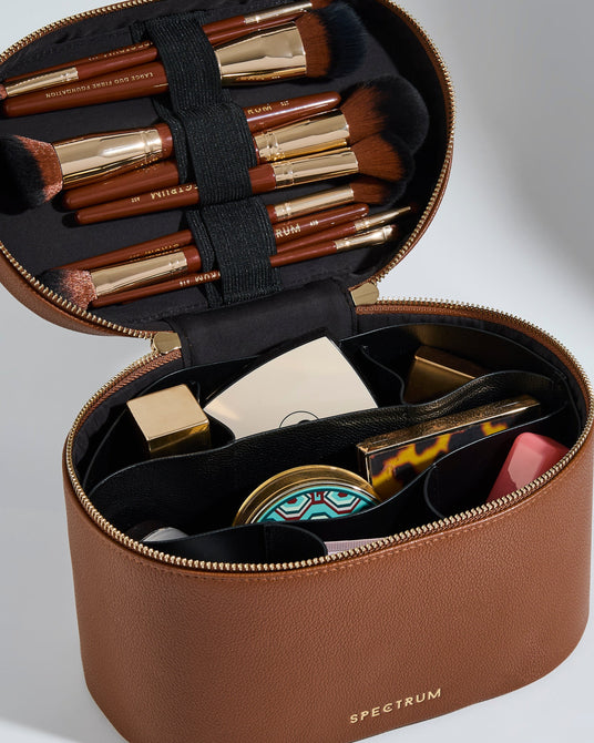 An open brown faux-leather makeup case with a black interior, holding multiple makeup brushes and cosmetic items. The case has a gold zipper and the brand name 'SPECTRUM' printed in gold on the front, set against a clean light gray background.