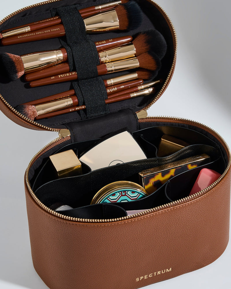 An open brown faux-leather makeup case with a black interior, holding multiple makeup brushes and cosmetic items. The case has a gold zipper and the brand name 'SPECTRUM' printed in gold on the front, set against a clean light gray background.